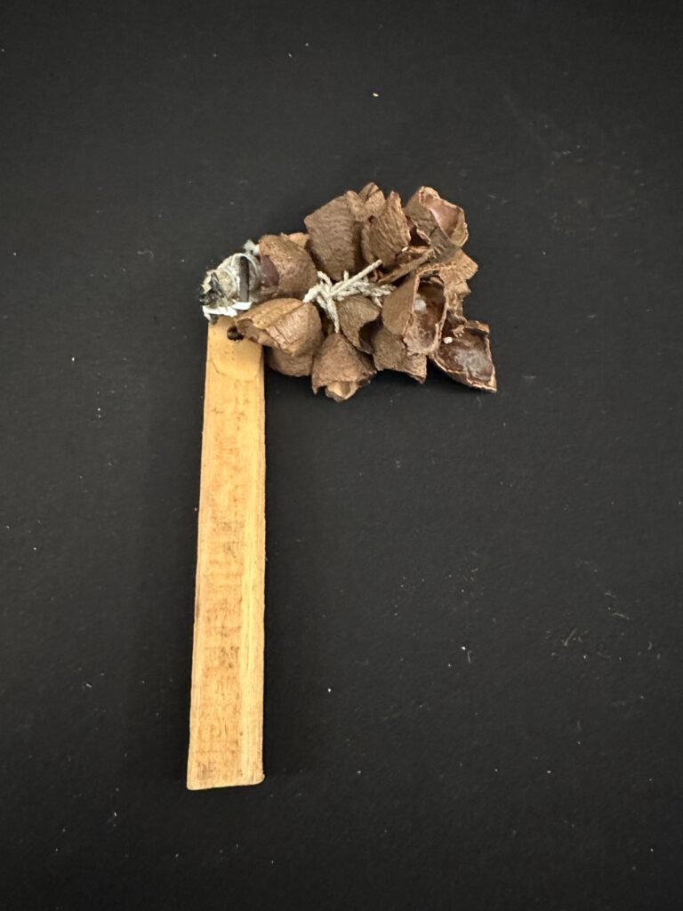 Brown Nutshell Shaker, 6in long, securely strung on wooden handle.